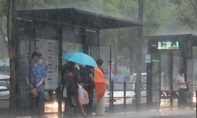 갑작스런 소나기가 내린 지난달 19일 오후 서울 종로구 숭인동 동묘앞역 버스정류장에서 시민들이 우산으로 쏟아지는 비를 막고 있다.
