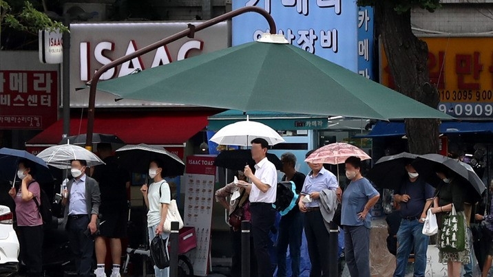 비가 오락가락한 날씨를 보인 2일 오후 서울 도심에서 우산을 쓴 시민들이 대형 그늘막 아래에 모여 신호를 기다리고 있다.
