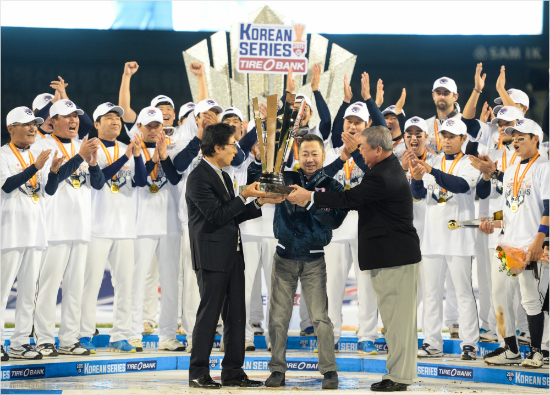 두산선수단이31일삼성과한국시리즈5차전에서승리,우승을확정한뒤구본능KBO총재(앞오른쪽부터)가우승컵을박정원구단주와김승영구단사장에게건네자환호하고있다.(잠실=두산베어스)