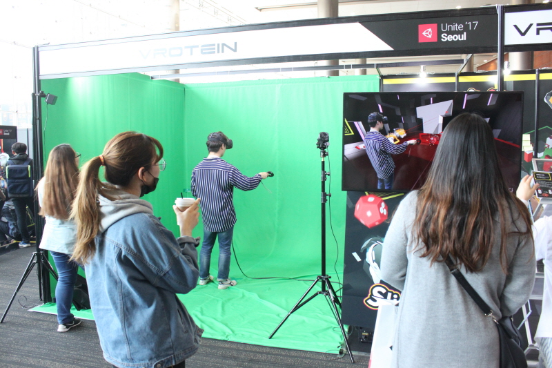 VR과 AR이 결합된 퍼즐 게임을 체험하고 있는 참가자와 이를 화면을 통해 지켜보는 관람객들의 모습.