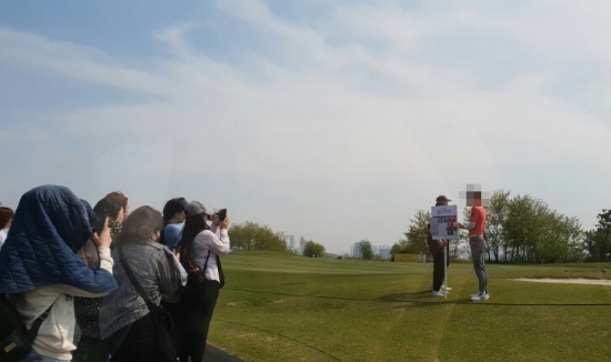 동반 플레이어들이 그린 위에서 플레이 중인 가운데, 한 셀러브리티가 홀로 팬들 앞에서 기념 사진을 찍고 있다.