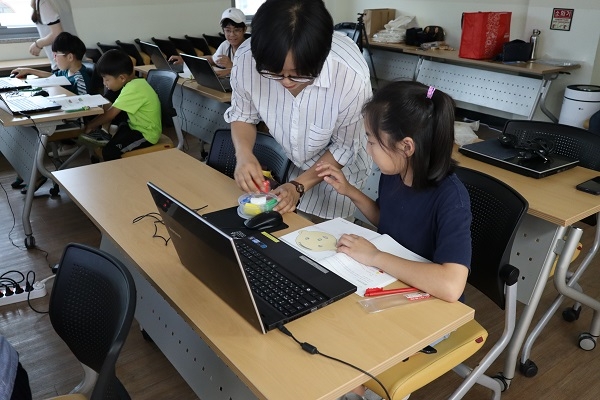 사진=의정부시 청소년문화의 집 어린이들이 지점토 인형의 얼굴에 손을 대면 표정이 바뀌는 프로그램을 코딩하고 있다.