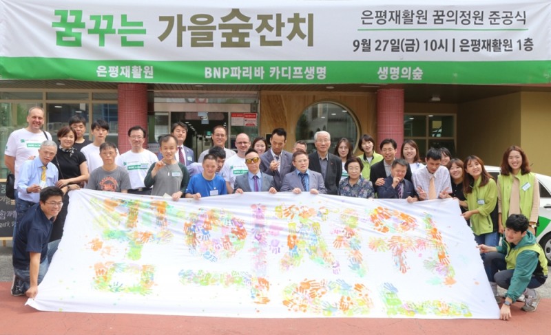 BNP파리바 카디프생명 임직원 자원봉사자, 은평재활원 이용인 및 관계자, 생명의숲 활동가들이 손바닥 페인팅을 찍어 함께 만든 친환경 현수막을 들고 단체 사진을 촬영하고 있다.