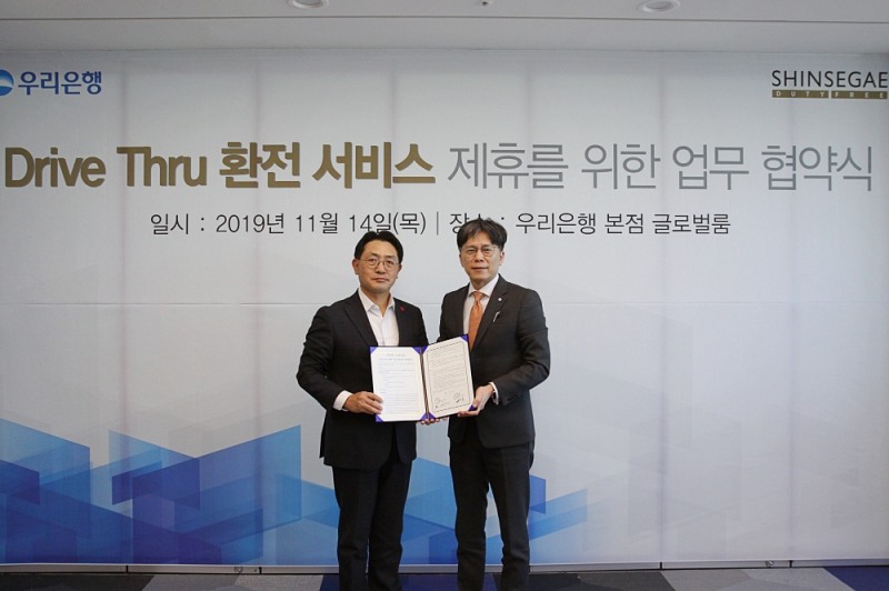 우리은행과 신세계 Drive Thru 환전 제휴를 위한 업무 협약 사진. 우리은행 황원철(오른쪽) 디지털금융그룹장과 문현규(왼쪽) 신세계면세점 마케팅 담당 상무가 기념촬영을 하고 있다.