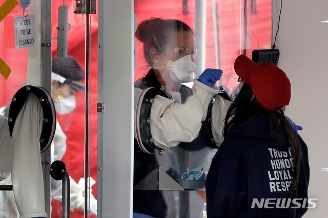 20일(현지시간) 미 매사추세츠주 첼시의 MGH 헬스케어 센터 밖에 있는 신종 코로나바이러스 감염증(코로나19) 테스트 장비인 워크스루에서 한 의료인이 한 여성의 검체를 채취하고 있다.