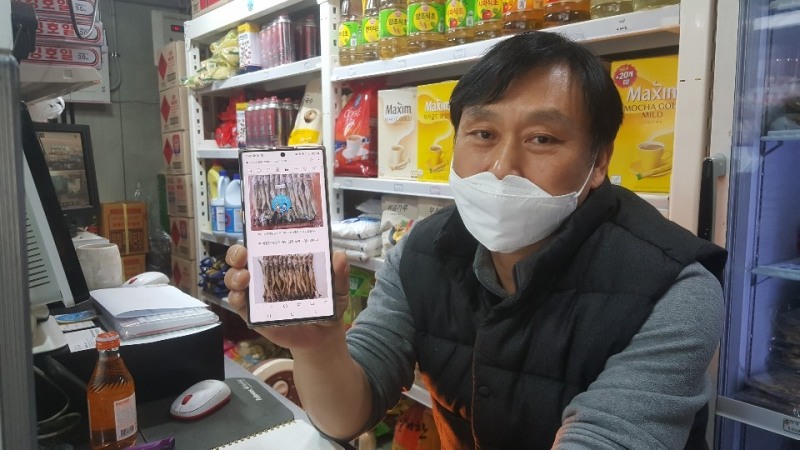 엄달용 사장이 현재 본인이 판매중인 건어물 제품을 스마트폰으로 보여주고 있다. 온라인(모바일)의 특성상 시간장소의 구애가 없기 때문에 전통시장을 살기를 가장 좋은 방법이라는 설명이다.