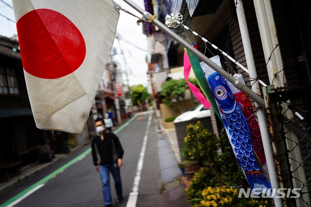 지난 5일 일본 도쿄에서 어린이날을 기념하기 위해 걸린 잉어 장식인 '고이노보리'와 일본 국기 뒤로 신종 코로나바이러스 감염증(코로나19) 예방을 위해 마스크를 쓴 시민이 걸어가고 있다.
