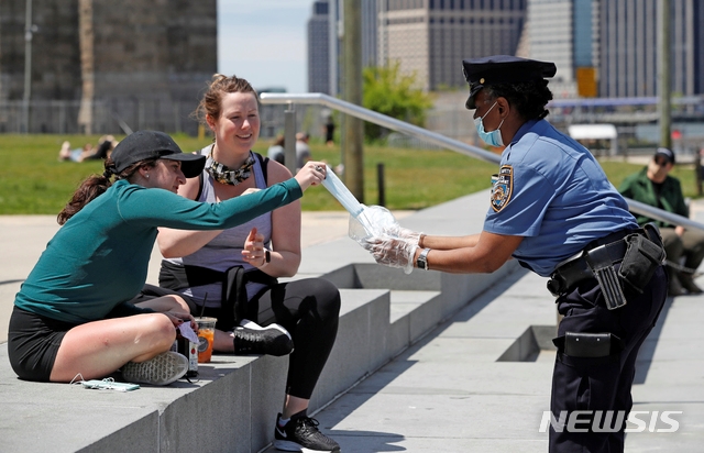 17일(현지시간) 미국 뉴욕에서 뉴욕시경(NYPD) 학교안전과 경찰이 신종 코로나바이러스 감염증(코로나19)을 막기 위한 마스크를 시민들에게 나눠주고 있다.