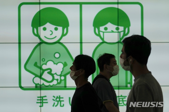 16일 일본 도쿄에서 마스크를 쓴 사람들이 코로나19 예방을 위해 손을 씻자는 현수막 앞을 걷고 있다.