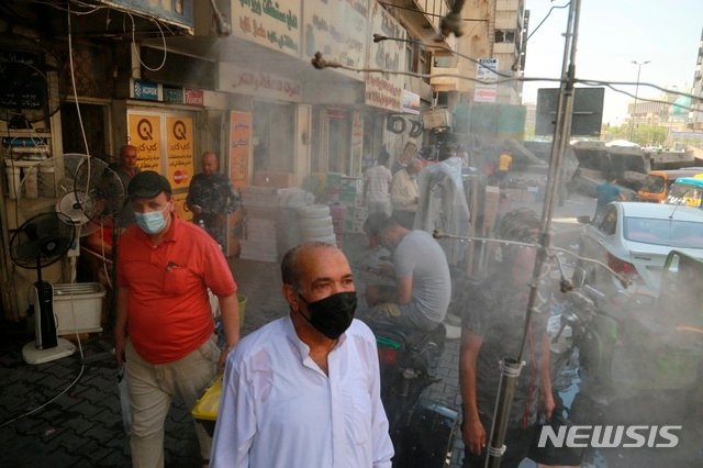 22일(현지시간) 이라크 바그다드에서 사람들이 분무 시스템이 설치된 길가에서 더위를 식히고 있다. 신종 코로나바이러스 감염증(코로나19)을 우려해 마스크를 착용한 사람들이 보인다.