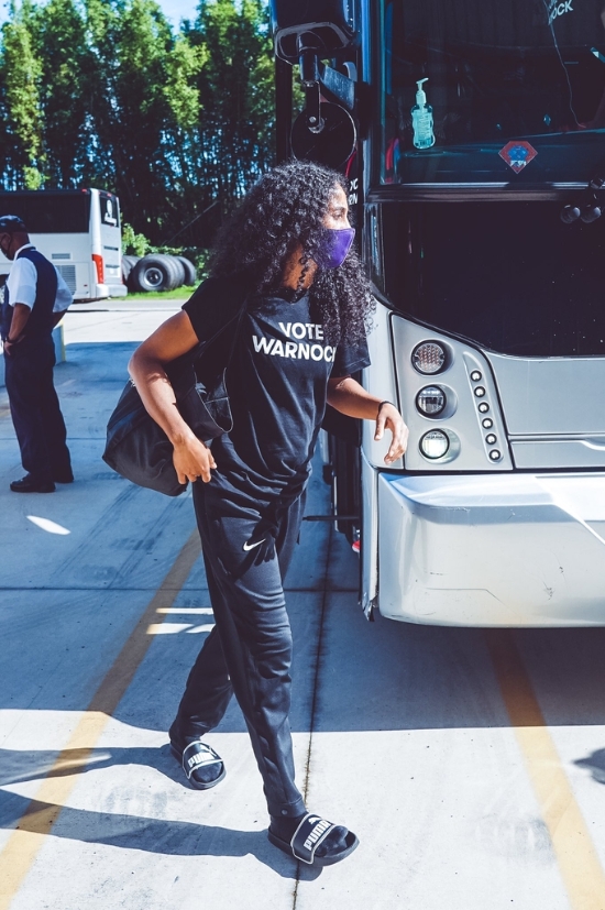 '워녹에게 투표하자'는 문구가 새긴 티셔츠를 입고 버스에서 내리는 디긴스 스미스.<br />[WNBA 피닉스 머큐리 구단 소셜 미디어 사진 캡처]