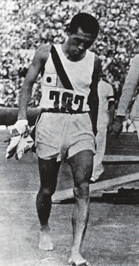 1936년 베를린올림픽 마라톤에서 우승한 손기정 선수가 신발을 벗고 여유롭게 걸어가고 있다. 고개를 푹 숙이고 걸어가는 모습이 더 슬퍼보인다.