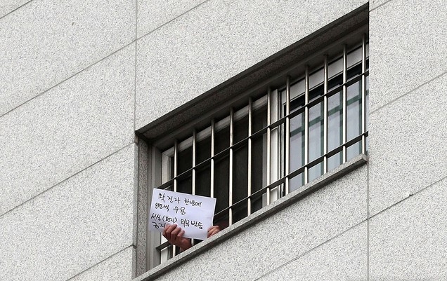 대규모 집단 감염이 발생한 서울 동부구치소에서 233명이 추가 확진돼 누적 확진자가 761명으로 집계된 29일 서울 송파구 동부구치소에서 한 수용자가 자필로 쓴 글을 취재진에게 보이고 있다. 종이에는 '확진자 한 방에 8명씩 수용, 서신(편지) 외부발송 금지'라고 적혀있다.