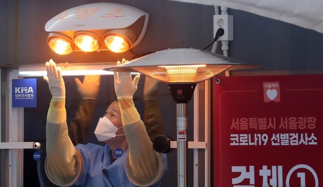 전국 곳곳에 한파 특보가 내려진 30일 오전 서울 중구 서울시청 광장에 설치된 신종 코로나바이러스 감염증(코로나19) 임시 선별검사소에서 한 의료진이 언 손을 온열기에 녹이고 있다.