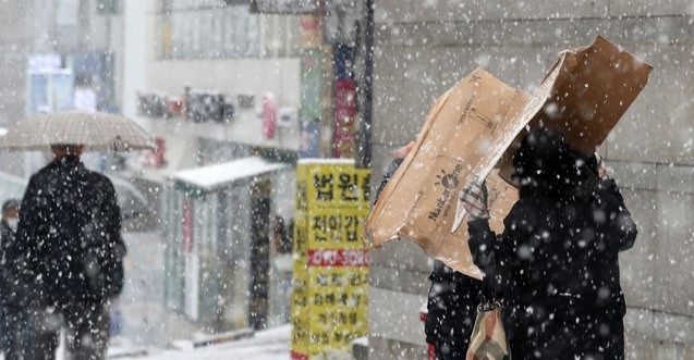 수도권을 포함한 중부지방에 눈이 내리기 시작한 지난 12일 오후 서울 서초구 인근에서 시민들이 상자를 쓰고 걸어가고 있다.