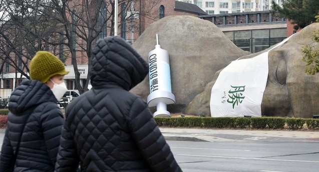 신종 코로나바이러스 감염증(코로나19) 백신 국내 접종 시작을 하루 앞둔 25일 오후 대구 달서구 진천동 선사유적공원 입구 원시인 조형물에 대형 주사기가 설치돼 눈길을 끌고 있다.