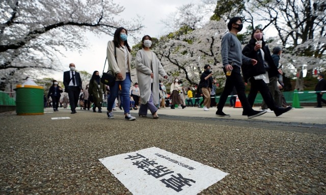 26일 일본 도쿄에서 마스크를 착용한 시민들이 코로나19 확산 방지를 위해 '친목 모임 금지'라는 안내문이 붙은 벚꽃로를 걷고 있다.