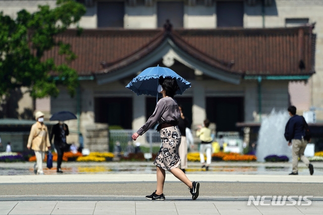 21일 일본 도쿄에서 코로나19의 확산을 막기 위해 마스크를 쓴 한 시민이 양산을 쓰고 거리를 걷고 있다. 