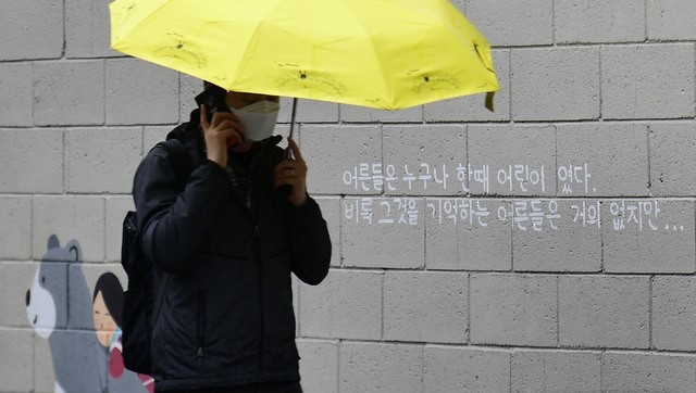 봄비가 내린 지난 12일 오후 대구 중구 삼덕동 벽화 길에서 한 시민이 우산을 쓴 채 걸어가고 있다. 최근 경북 구미에서 3세 여아가 홀로 방치된 채 사망하는 등 아동학대 사건이 끊이지 않는 가운데 벽화에 적힌 문구가 시선을 사로잡는다.