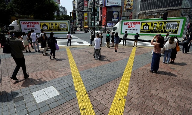 14일 일본 도쿄에서 코로나19 주의 안내판을 부착한 트럭들이 마스크를 쓴 시민들이 있는 거리를 지나고 있다. 도쿄도는 이날 854명의 코로나19 신규 확진자가 발생했다고 밝혔다.