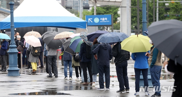 지난 21일 오전 서울 중구 서울역광장에 마련된 코로나19 중구임시선별검사소에서 시민들이 검사를 받기 위해 우산을 쓰고 줄 서 있다.