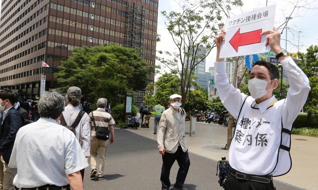 일본 수도 도쿄 시내에 설치된 코로나19 대량 접종센터앞에서 24일 보건당국 직원이 시민들에게 길 안내를 하고 있다. 일본 정부는 이날 자위대 군의관과 간호장교를 동원해 도쿄도와 오사카에서 고령자를 대상으로 백신 투여를 시작했다.