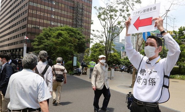 일본 수도 도쿄 시내에 설치된 코로나19 대량 접종센터앞에서 24일 보건당국 직원이 시민들에게 길 안내를 하고 있다. 일본 정부는 이날 자위대 군의관과 간호장교를 동원해 도쿄도와 오사카에서 고령자를 대상으로 백신 투여를 시작했다.