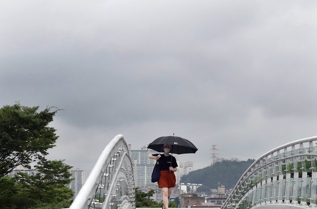 비가 오고 바람이 부는 3일 오후 인천시 남동구 중앙공원 보행육교에서 우산을 쓴 시민이 비구름 머금은 하늘을 배경으로 걸어가고 있다.
