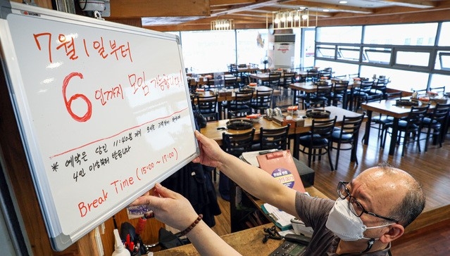 새로운 사회적 거리두기 시행을 하루 앞둔 30일 오후 서울 시내 한 식당에서 점주가 '7월 1일부터 6인 모임 가능' 안내판을 거치하고 있다. 내달 1일부터 적용되는 새로운 사회적 거리두기는 수도권 지역 음식점 및 실내체육시설, 유흥시설 등의 영업 제한 시간이 밤 12시까지 늘어나고 사적 모임 인원이 2주간 최대 6인까지 허용된다.