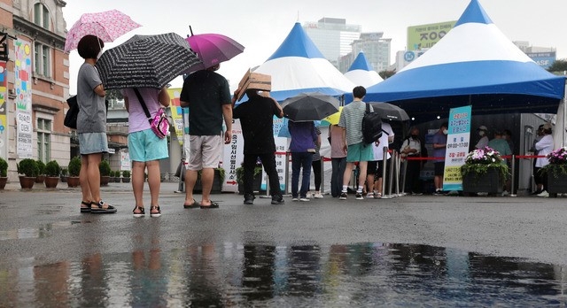 지난 10일 오전 서울 중구 서울역광장에 마련된 중구 임시선별진료소에서 내리는 소나기속 검사를 받으려는 시민들이 길게 줄지어 서 있다.