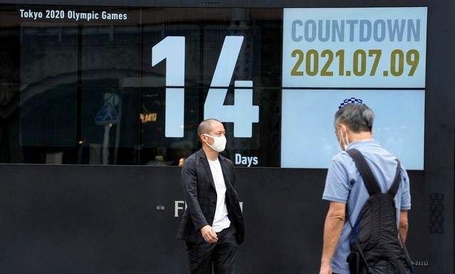 도쿄올림픽이 2주일 앞으로 다가온 가운데 9일 일본 도쿄 신바시역 부근에서 코로나19 예방을 위해 마스크를 착용한 시민들이 '올림픽 카운트다운 시계' 앞을 지나고 있다.