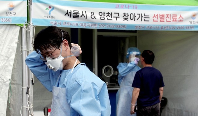 지난 21일 오후 서울 양천구 파리공원 안에 설치된 코로나19 임시선별검사소에서 의료진이 생수를 목에 대며 더위를 식히고 있다.