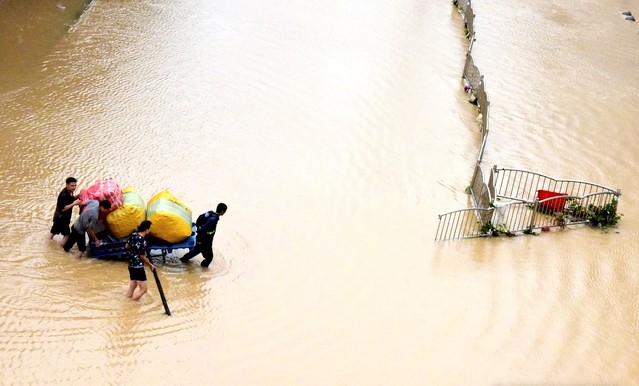 21일 중국 허난성 정저우에서 시민들이 귀중품 등을  수레에 싣고 침수 거리를 건너고 있다. 중국군은 정저우 인근 댐이 홍수로 균열이 생기자 수압을 낮추기 위해 제방을 폭파하기도 했다. 지금까지 홍수로 최소 25명이 숨지고 7명이 실종된 것으로 알려졌다.