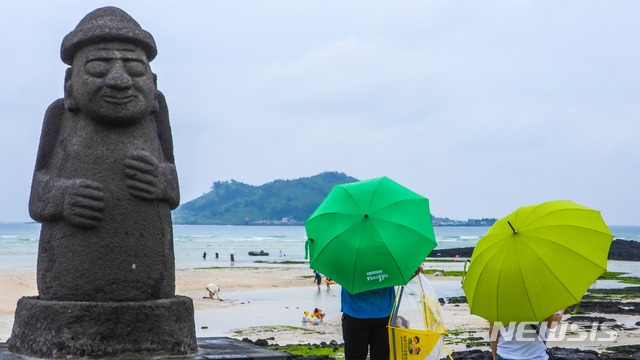 제주시 한림읍 금릉해수욕장에 우산을 쓴 관광객들이 바다를 응시하고 있다.