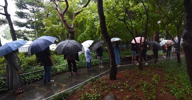 비가 내리고 있는 지난 24일 대구 중구 국채보상운동기념공원 코로나19 임시선별검사소에서 시민들이 검사를 받기 위해 우산을 쓰고 긴 줄을 서고 있다.