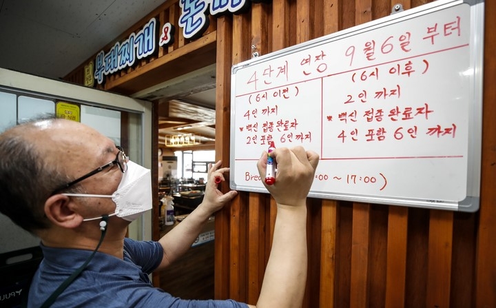 지난 3일 오후 서울 종로구에 위치한 한 식당에서 식당 주인이 거리두기 관련 내용을 적고 있다. 정부가 현행 사회적 거리 두기 단계를 10월3일까지 한 달 연장하되, 예방접종 완료자 사적 모임 예외 적용을 확대하기로 했다. 다만 접종 완료자 포함 수도권 등 4단계 지역은 식당·카페·가정에서 6명까지, 3단계 이하 지역은 모든 사적모임이 8명까지 가능하며, 4단계 지역 식당·카페의 매장내 영업시간은 오후 10시로 다시 1시간 늘어나는 등 방역수칙이 일부 완화됐다.