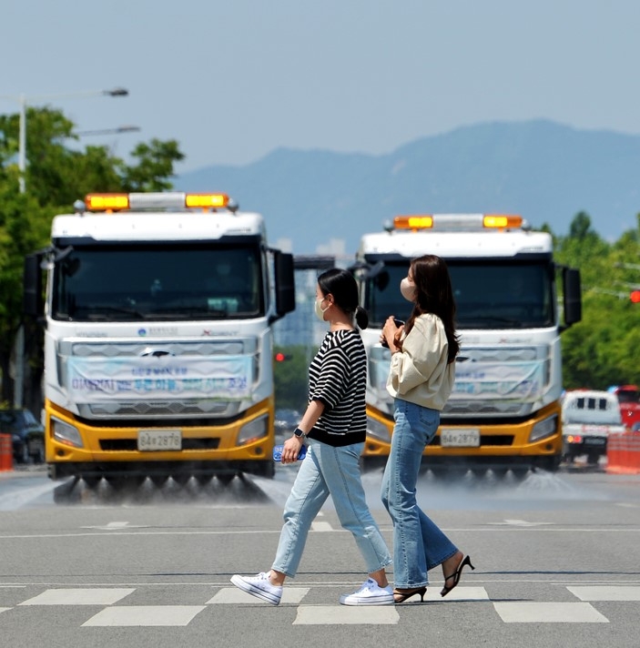한 낮 더위가 30도에 육박한 지난 24일 오후 광주 서구 상무누리로에서 서구청 살수차가 물을 뿌려 온도를 낮추고 있는 가운데 시민들이 횡단보도를 걷고 있다.
