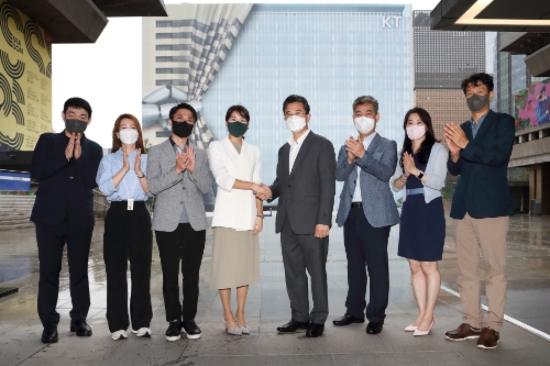 KT 전략기획실장 김채희 전무(좌측 네번째)와 서울시 주용태 문화본부장(우측 네번째)이 양측 관계자들과 함께 광화문 West 사옥 공사 가림막을 배경으로 세종문화회관 중앙계단에서 업무협약 체결 기념 촬영하는 장면