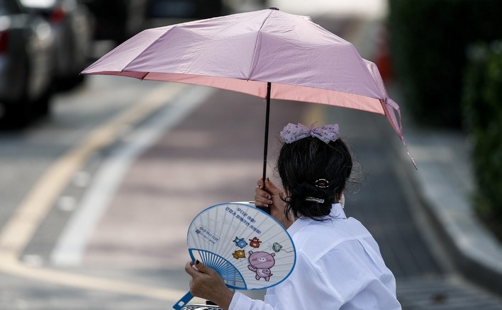 지난 19일 오전 서울 종로구 광화문네거리에서 한 시민이 양산과 부채로 더위를 피하고 있다.