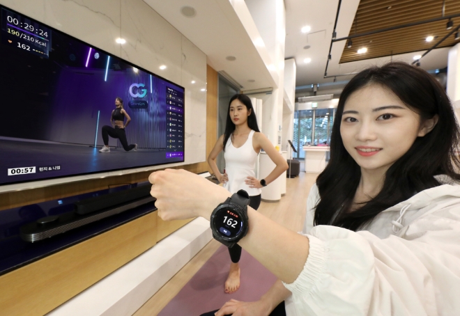LG유플러스는 IPTV용 서비스인 ‘U+홈트Now’와 스마트워치를 연동해 운동 중 생체정보를 확인하고 이용자간 경쟁하며 운동할 수 있는 신개념 홈트 서비스 ‘코코어짐’을 선보였다고 6일 밝혔다. 사진은 LG유플러스 모델이 U+tv와 갤럭시워치를 연동해 코코어짐 서비스를 이용하고 있는 모습. (사진 = LG유플러스 제공)