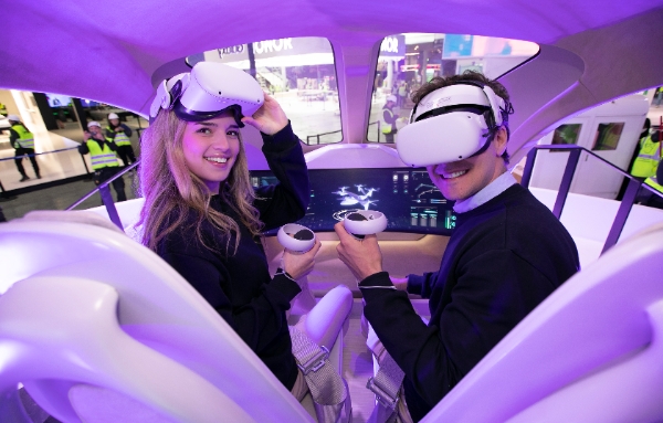 SKT 전시관에서 현지 모델들이 UAM 모형에 탑승해 2030년의 서울을 배경으로 비행하는 서비스를 체험하고 있는 모습