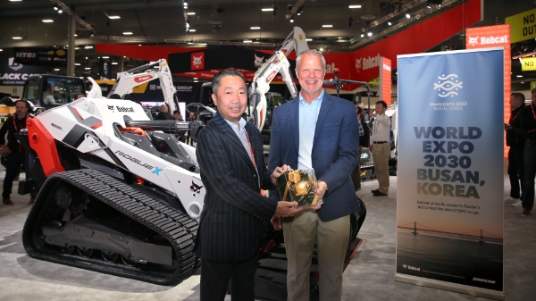 박정원 두산그룹 회장이 미국 라스베이거스에서 열린 ‘콘엑스포 2023’의 두산밥캣 부스에서 무인 전기 콘셉트 로더 ‘로그 X(Rogue X)’ 와 부산엑스포 유치를 기원하는 배너 앞에서 마이크 볼웨버 북미 지역장에게 두산일두(斗山一斗)를 전달하고 있다. / 사진제공:두산그룹