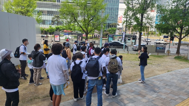 풀무원과 SSG닷컴의 지구의날 플로깅 이벤트에 참여한 참가자들이 용산기지 둘레길 산책 문화행사 인솔자의 설명을 듣고 있는 모습