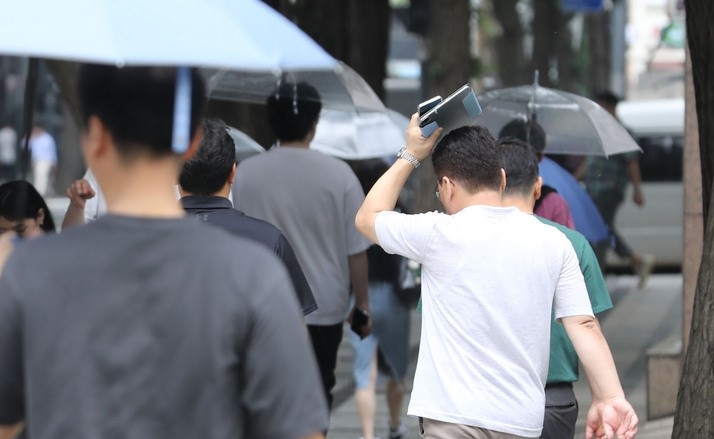 지난 8일 오후 서울 종로구 청계천 인근에서 한 시민이 소지품으로 비를 피하고 있다.