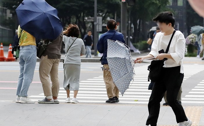 소나기가 내린 지난 10일 서울 광화문 네거리에서 한 시민이 강풍에 우산을 붙잡는 모습.