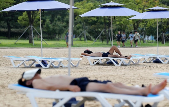 전국 대부분 지역에 폭염특보가 발효된 지난 14일 서울 송파구 잠실한강공원에 조성된 '해변쉼터' 파라솔 아래서 시민들이 더위를 피하고 있는 모습.