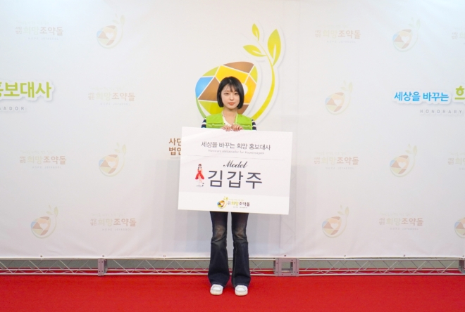 사진 = 김갑주가 희망조약돌 포토월 앞에서 기념포즈를 취하고 있다. 출처: 희망조약돌