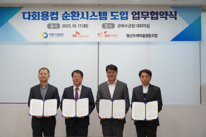 SK텔레콤(SKT)은 세종특별자치시시설관리공단, 사회적기업 행복커넥트, 왕산두레마을협동조합과 함께 은하수공원에 다회용 컵 순환 시스템을 도입하기 위한 업무협약을 체결했다고 18일 밝혔다. 사진은 지난 17일 은하수공원에서 (좌측부터)박대호 행복커넥트 상임이사, 조소연 세종시설공단 이사장, 이준호 SK텔레콤 ESG추진담당, 이진일 왕산두레마을협동조합 이사장이 업무협약을 체결하는 모습. (사진 = SKT 제공)