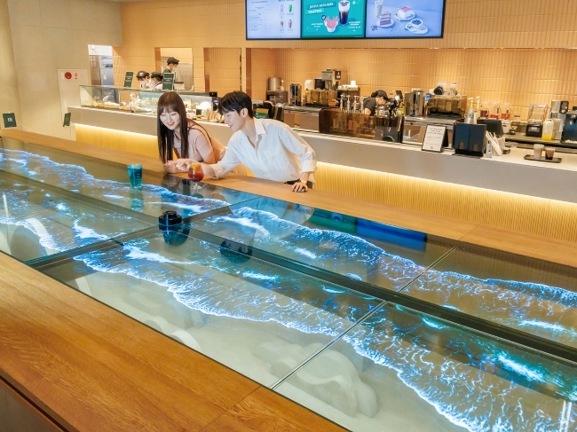 LG디스플레이 모델이 스타벅스 '더여수돌산DT점'에서 55인치 투명 OLED 12대를 이어붙인 초대형 투명 OLED 테이블을 체험하고 있다.
