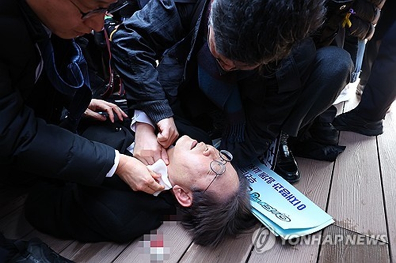 더불어민주당 이재명 대표가 2일 부산 가덕도 신공항 부지를 둘러본 후 기자들과 문답을 진행하던 중 왼쪽 목 부위에 습격을 당해 피를 흘린 채 쓰러져 있다. (사진=연합)